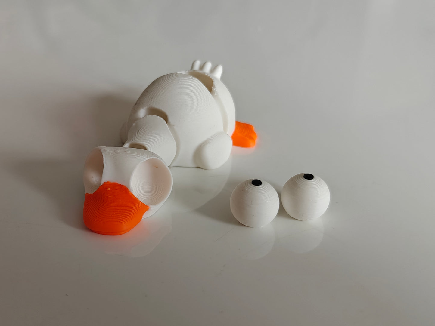 Small goofy goose figure with googly eyes sitting on a wooden desk next to a keyboard