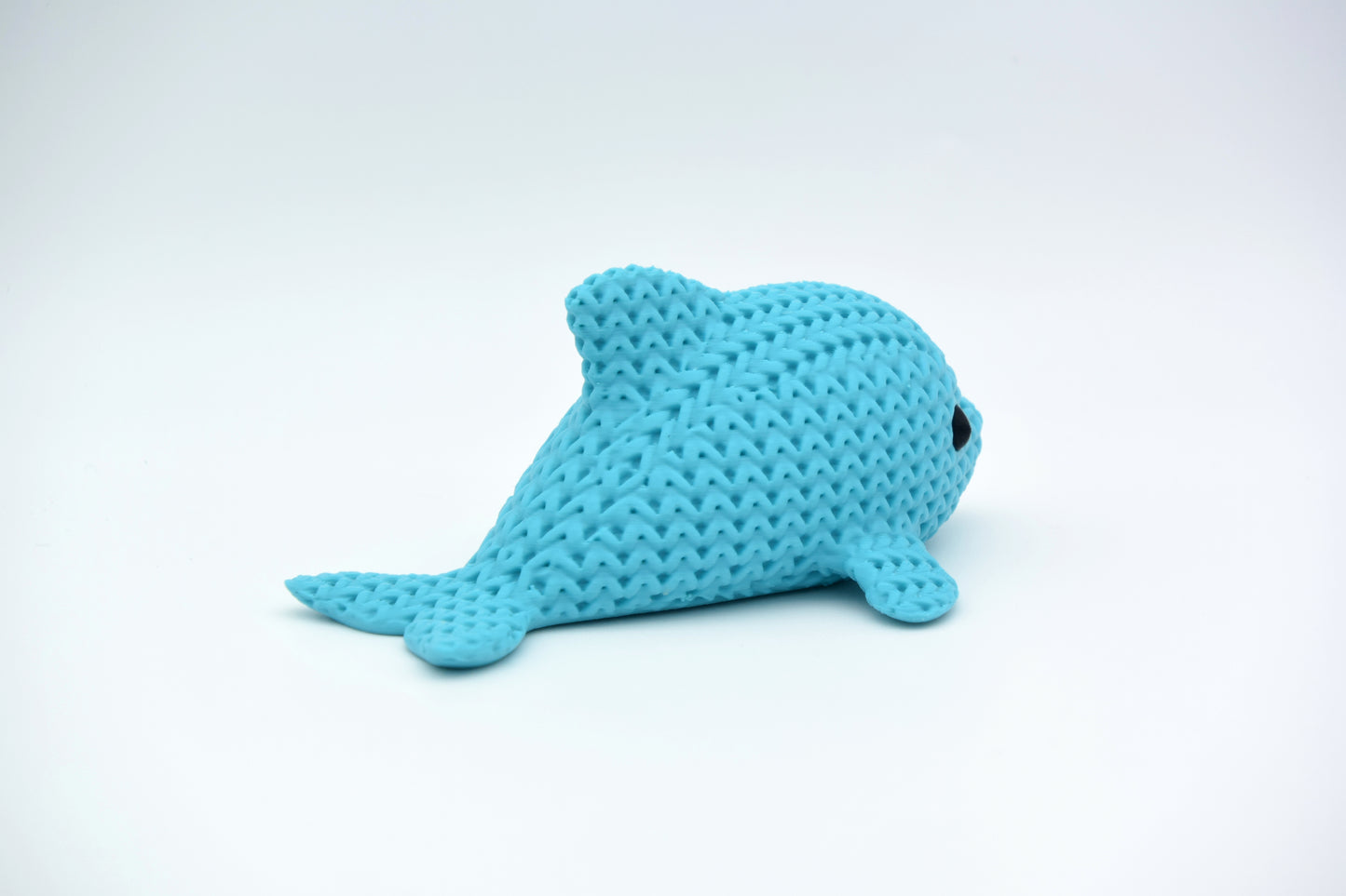 Close-up of a small knitted dolphin figurine with soft crochet-textured surface and round inset eyes