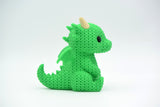 Close-up of a knitted dragon figurine with crochet-texture surface, shown against a light background