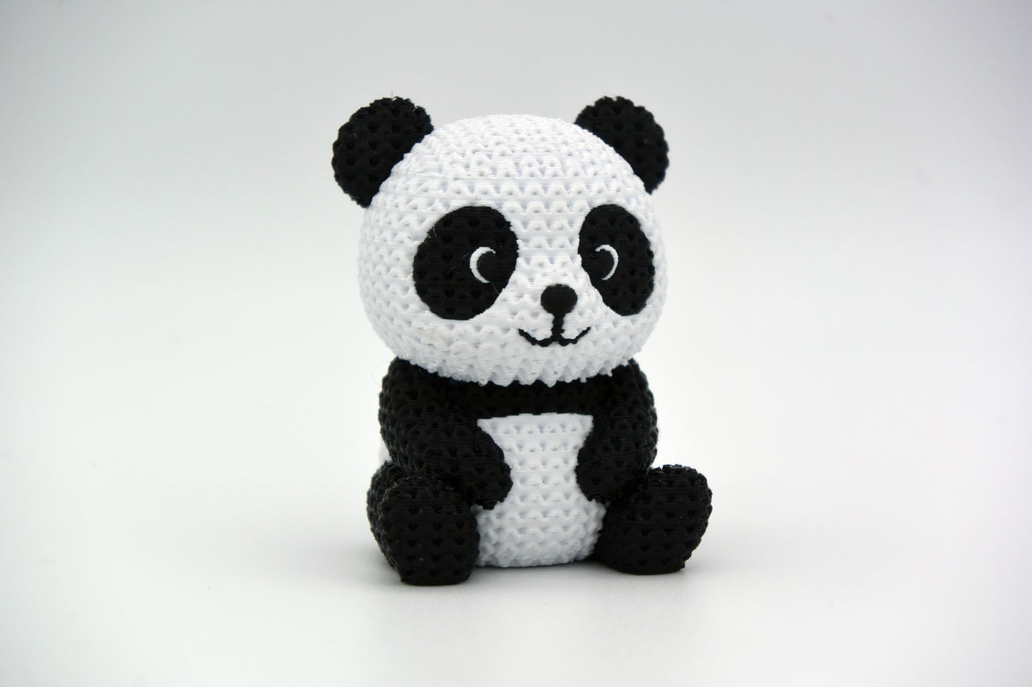 Knitted panda figure styled on a wooden shelf next to plants and neutral home decor