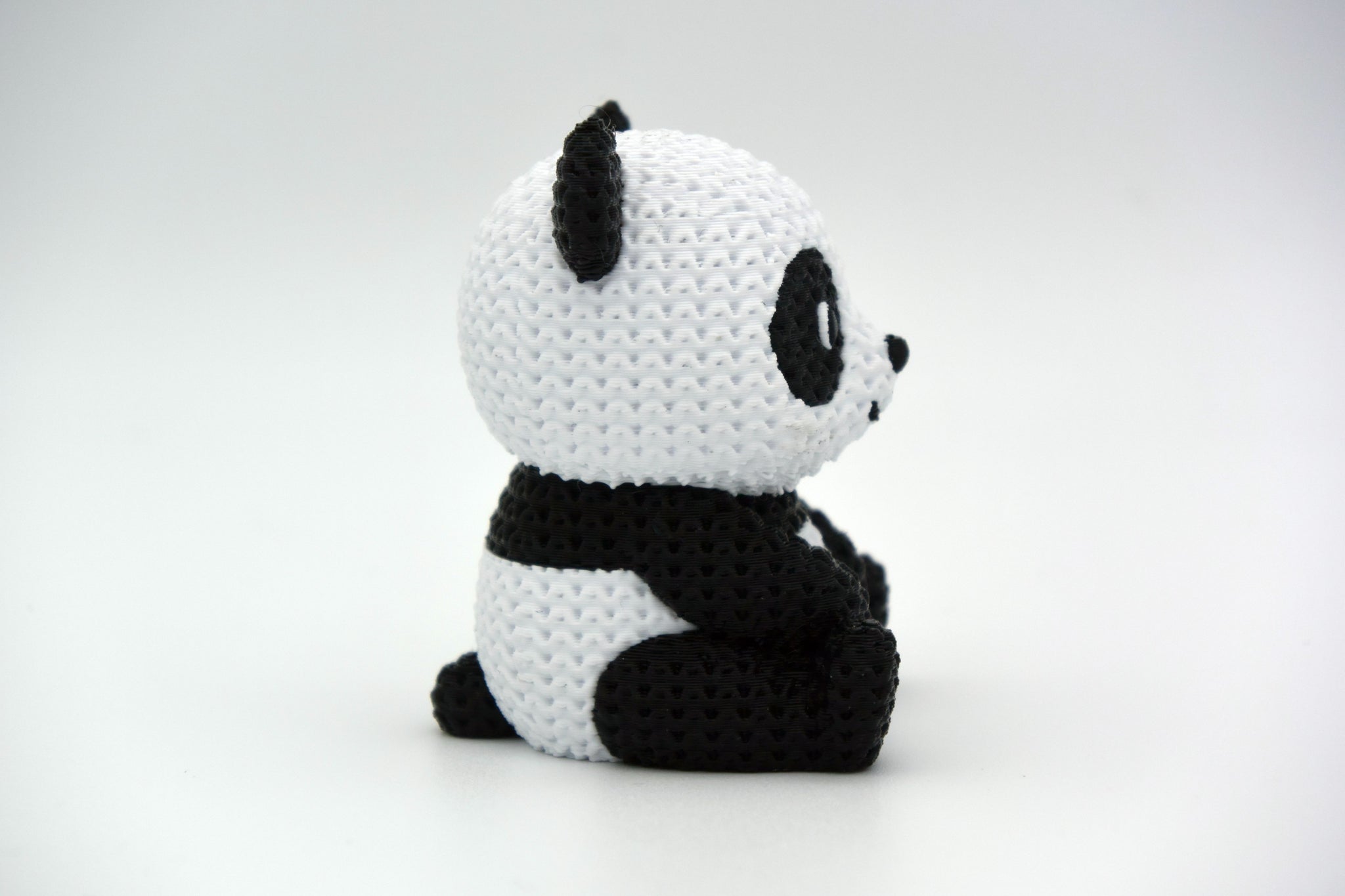 Close-up of a knitted panda figurine showing black and white crochet-look texture, small decorative object