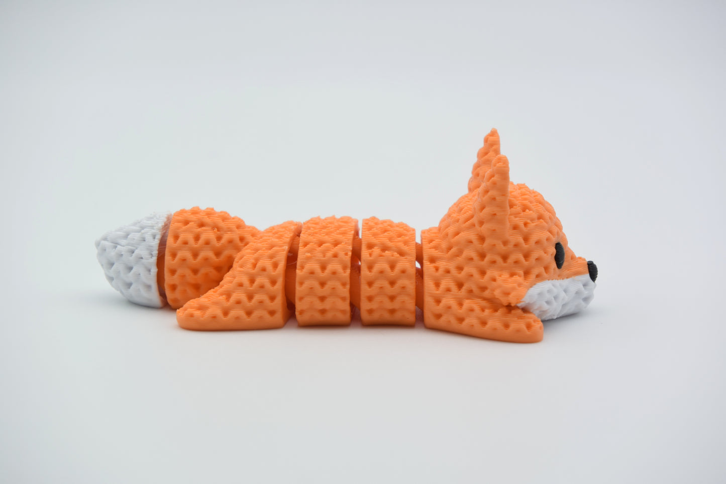 Small knitted articulated fox resting on a wooden shelf beside books and a candle in a cosy Scandinavian interior