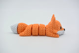 Small knitted articulated fox resting on a wooden shelf beside books and a candle in a cosy Scandinavian interior