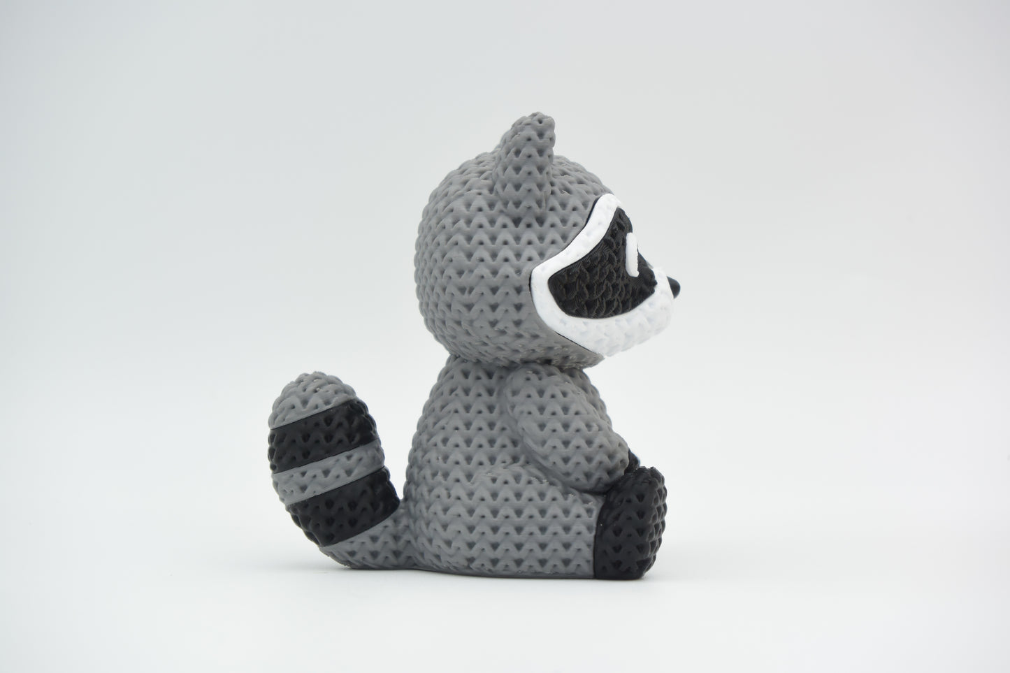 Knitted raccoon decorative figure placed on a wooden shelf beside books and a small plant