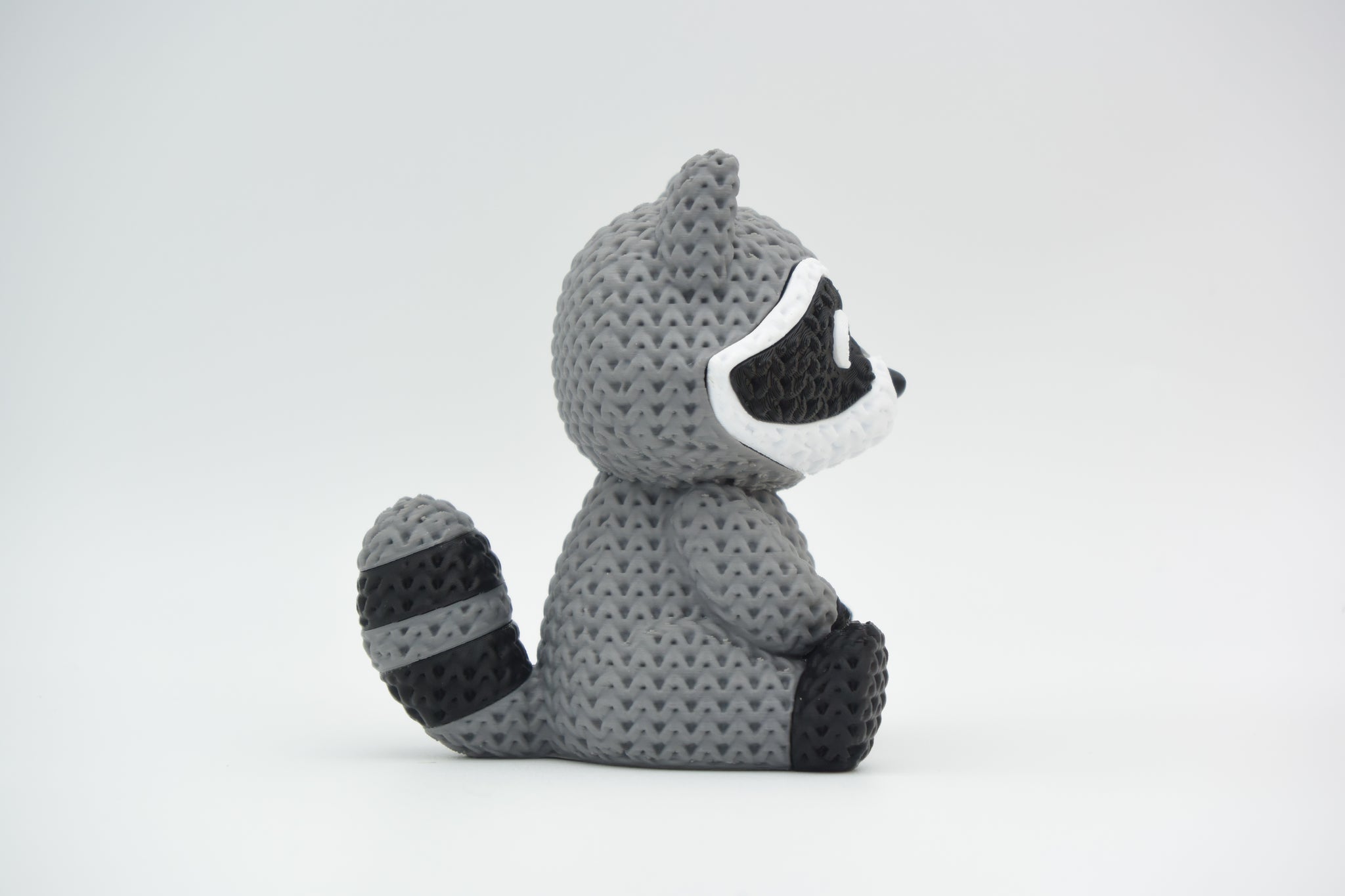 Knitted raccoon decorative figure placed on a wooden shelf beside books and a small plant