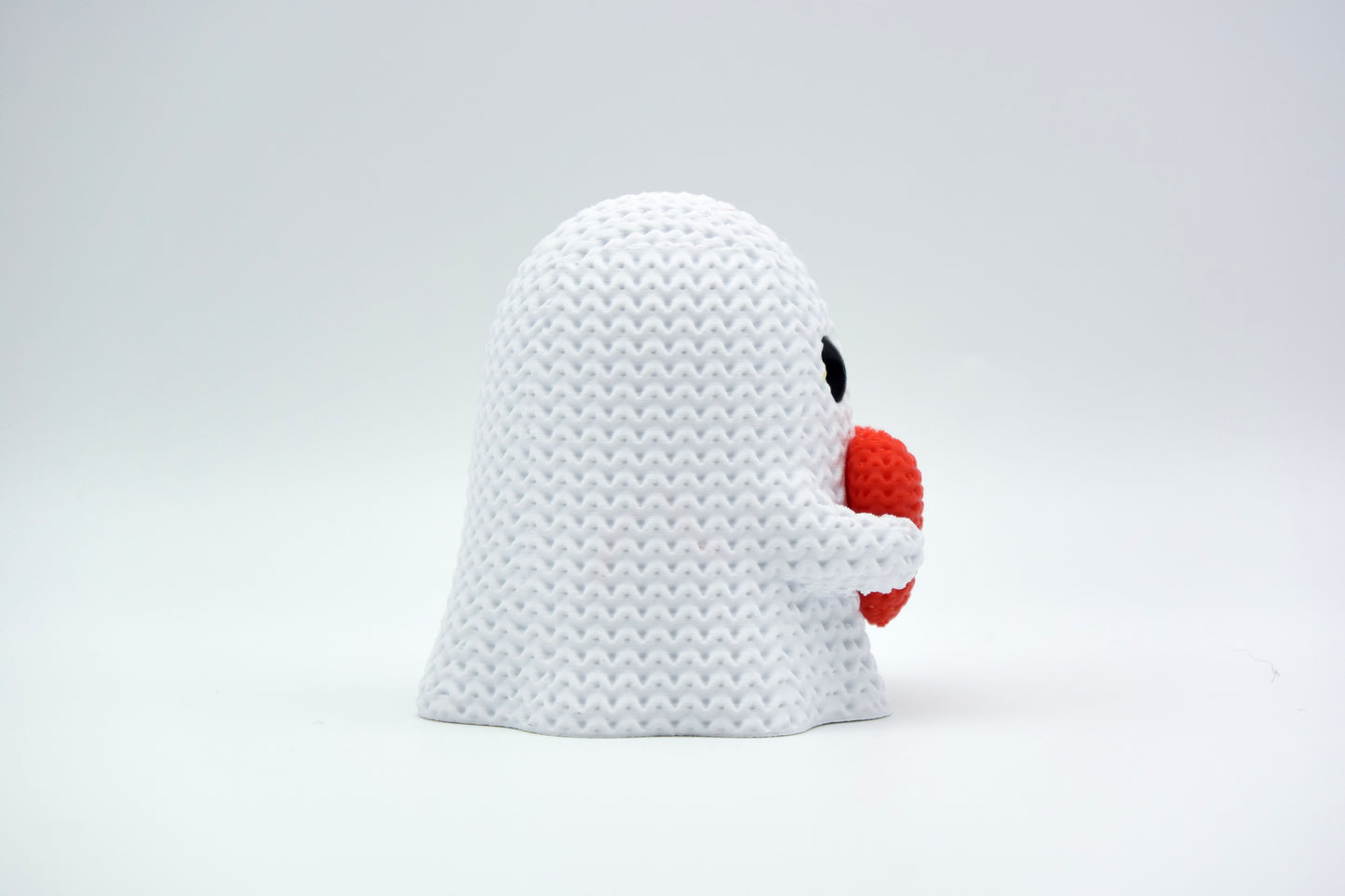 Small knitted ghost decoration with heart styled on a wooden shelf among autumn home decor