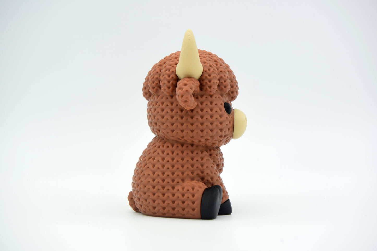 Close-up of a knitted highland cow figurine with a textured crochet-look coat and small sculpted horns
