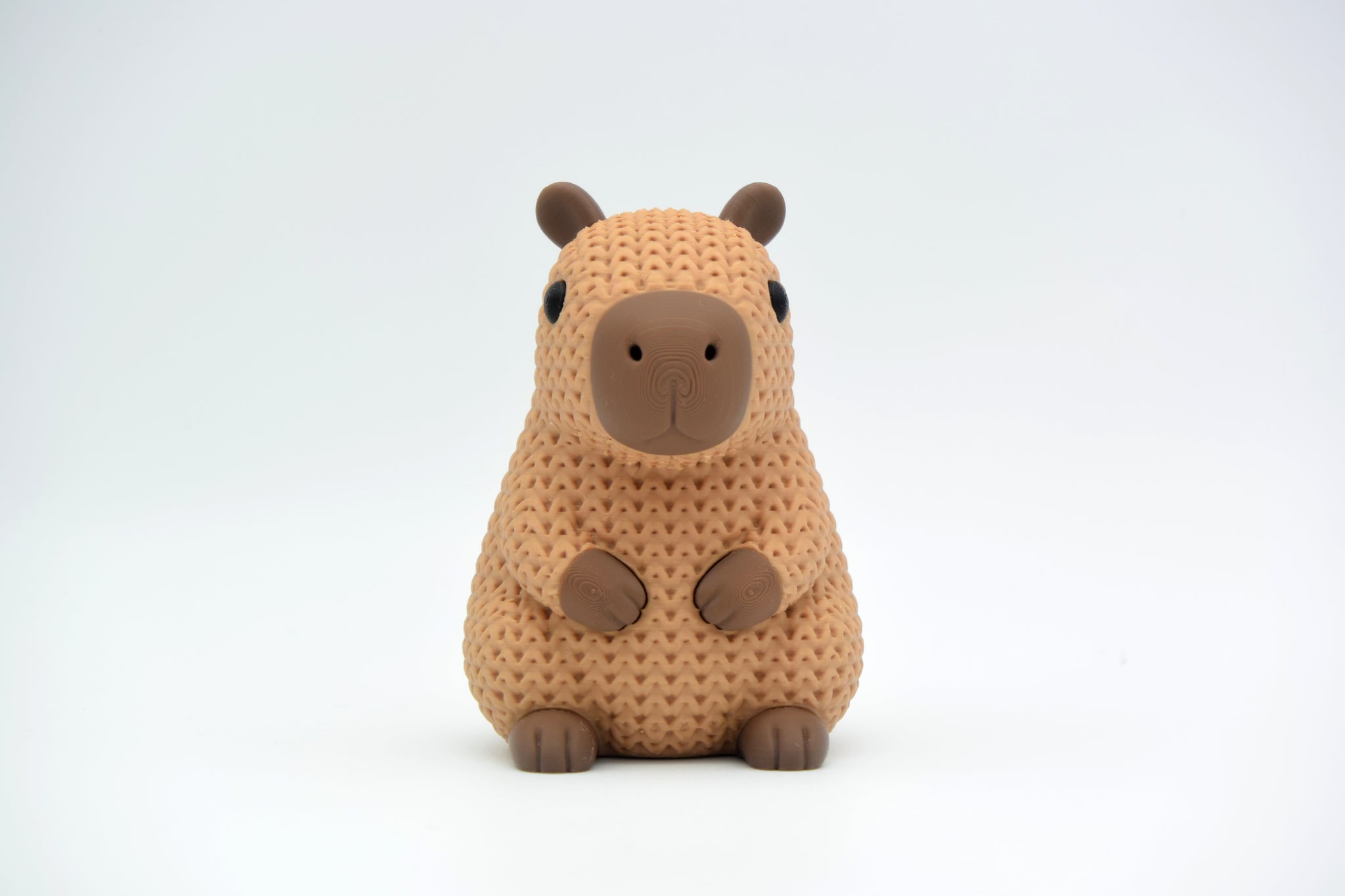 Close-up of a knitted capybara figure with soft crochet texture in warm brown tones, on a white surface