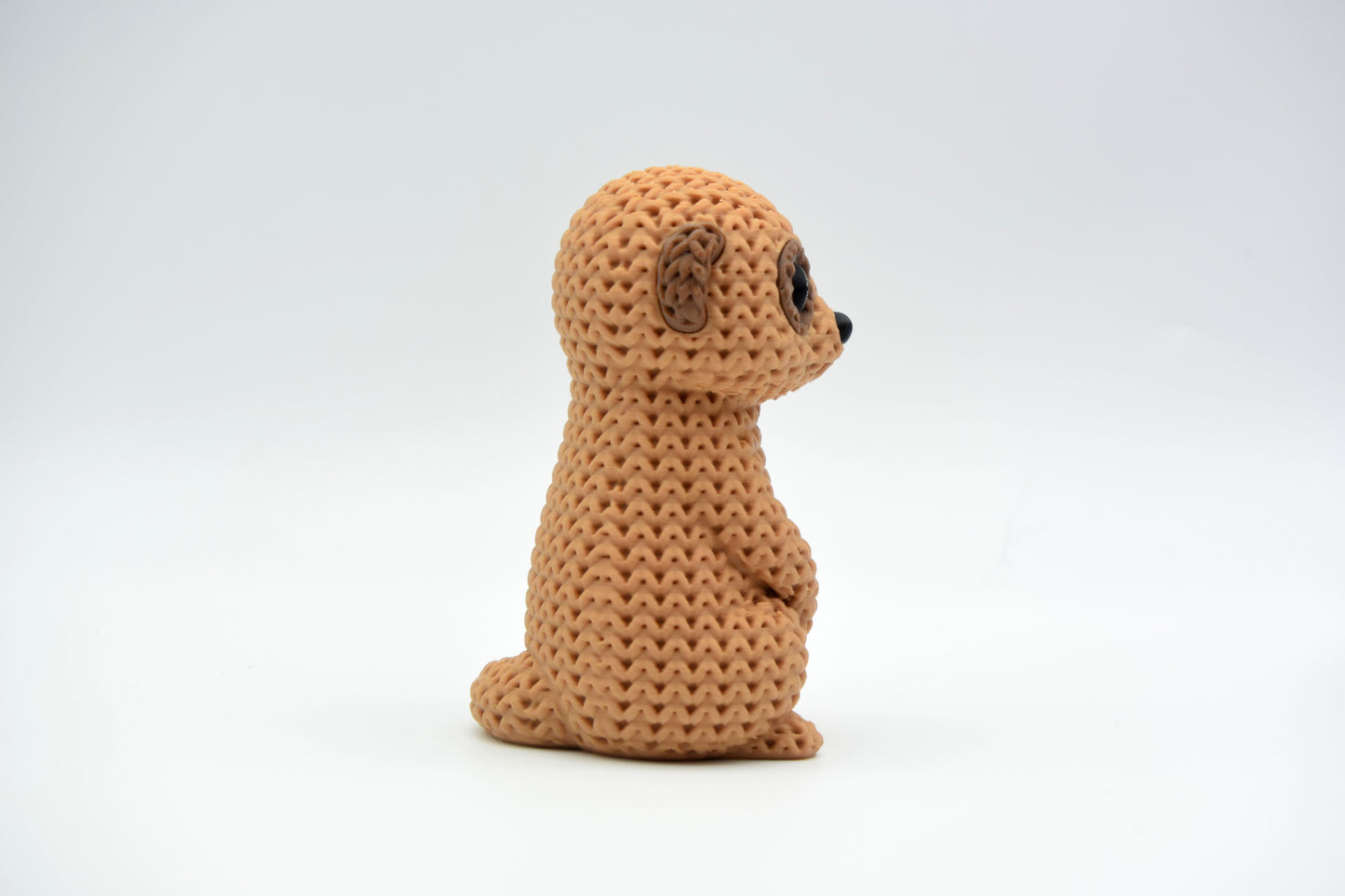 Close-up of a knitted meerkat figurine with a crochet-texture surface, standing upright on a white background